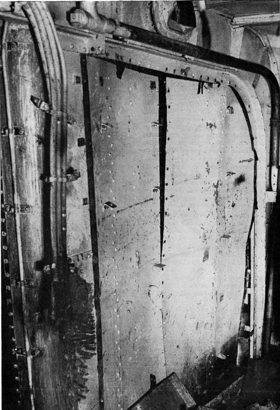 Figure 13-B. Another common type of damage. Observe the warped bulkhead, the severed electric cables, and the damaged vent duct. The integrity of this boundary has been seriously impaired.